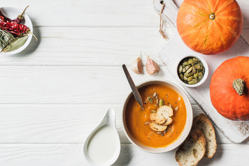 flat lay with pumpkins, garlic, rusks and bowl with homemade pumpkin cream soup on table
