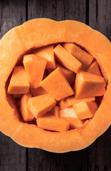 elevated view of raw pumpkin with pieces inside on wooden table