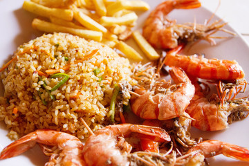 Shrimps on white plate over wooden table, served with rise and french fries, top view. Seafood concept.Selective focus.