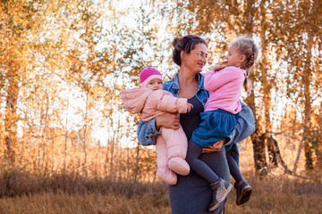 The concept of livestyle and family outdoor recreation in autumn. A young  mother  holding her daughters and enjoying nature, posing and talking to them on the back of a background of autumn field 