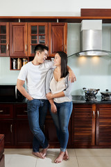 Happy Asian boyfriend and girlfriend hugging and looking at each other in new apartment