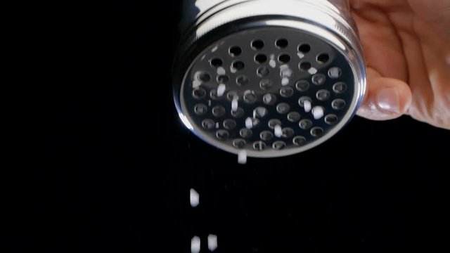 Salt flies straight into the camera on black background. Slow motion.
