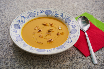 Delicious creamy pumpkin soup made from hokaido pumpkin with roasted seeds and olive oil served in the rustic deep plate with the spoon and red and green napkin. 