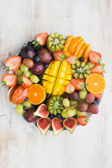 Variety of cut fruits and berries platter, strawberries blueberries, mango orange, apple, grapes, kiwis on the white wood background, copy space for text, vertical, top view, selective focus