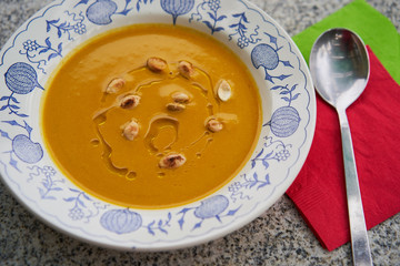 Close up picture tasty creamy pumpkin soup made from hokaido pumpkin with roasted seeds and olive oil served in rustic deep plate with the spoon and red and green napkin. 