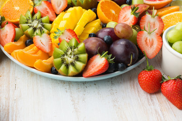 Variety of cut fruits and berries platter, strawberries blueberries, mango orange, apple, grapes, kiwis on the white wood background, copy space for text, close up, selective focus