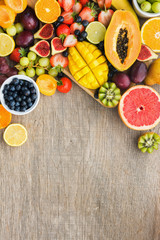 Top view of assorted fruits, strawberries blueberries, mango orange, grapefruit, banana papaya apple, grapes, kiwis on the grey wood background, copy space for text, vertical, selective focus