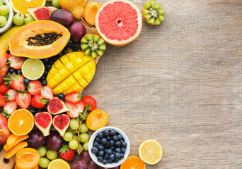 Top view of healthy fruits, strawberries blueberries, mango orange, grapefruit, banana papaya apple, grapes, kiwis, figs on the grey wood background, copy space for text, selective focus