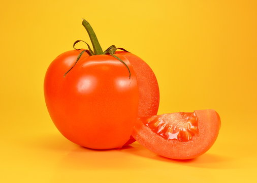 Red tomato with cut slice on yellow background