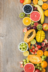 Top view of rainbow colored fruits, strawberries blueberries, mango orange, grapefruit, banana papaya apple, grapes, kiwis on the grey wood background, copy space for text, selective focus