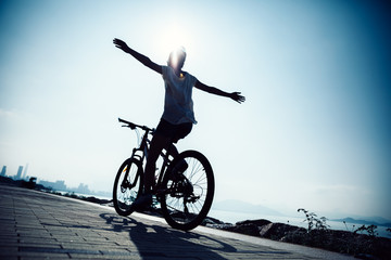 Fototapeta na wymiar Hands free cycling woman riding Mountain Bike on sunrise seaside