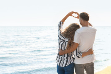 Cute young couple making heart with their hands on sea shore