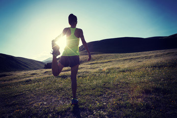 Young fitness woman trail runner warming up at grassland