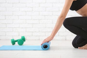 Young woman rolling yoga mat indoors