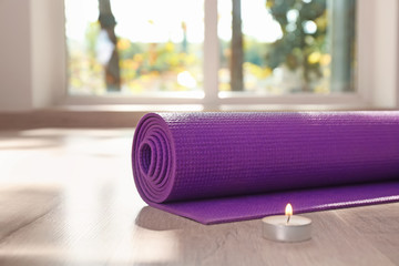 Yoga mat and  burning candle on floor