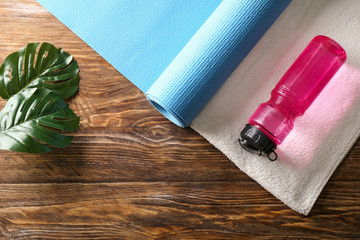 Yoga mat with bottle of water and towel on wooden background