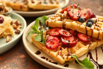 Delicious waffles with chocolate syrup and berries on plate, closeup