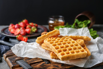 Wooden board with delicious Belgian waffles on table