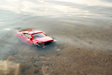 red toy car submerged in the water, drowned in the pond facing us, the accident in the summer