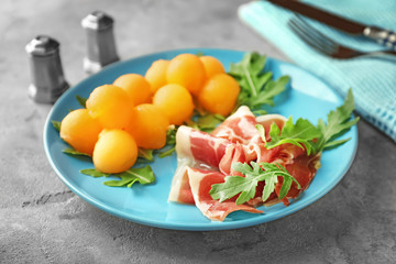 Plate with delicious melon balls and prosciutto on table