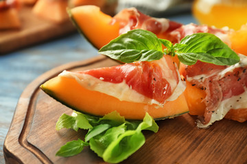 Delicious melon with prosciutto and basil on wooden board, closeup