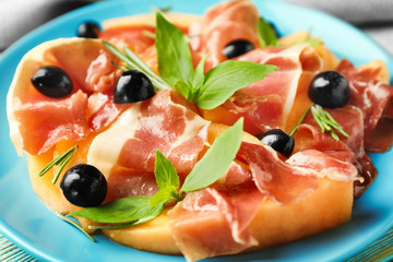 Delicious melon, prosciutto and olives on plate, closeup