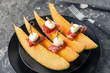 Delicious canape with melon, prosciutto and mozzarella on plate, closeup