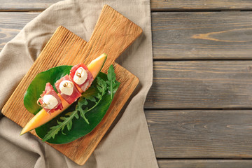 Delicious canape with melon, prosciutto and mozzarella on wooden board, top view