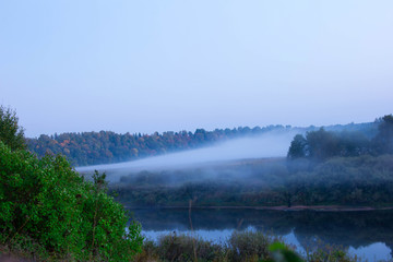 Amazing scenery of a river bank and field with starting fog. Evening landscape 