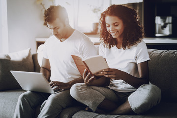 Couple With Laptop And Book Sitting On The Couch.