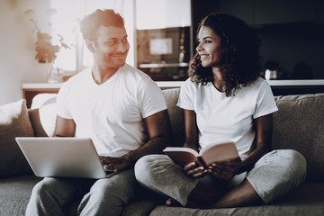 Couple With Laptop And Book Sitting On The Couch.