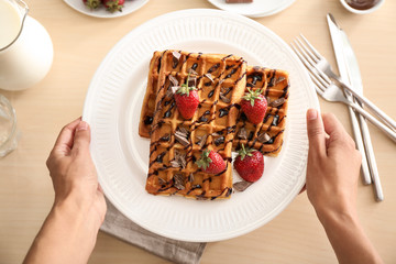Woman holding plate with tasty waffles and berries over table, top view