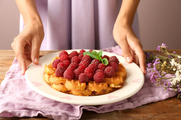 Woman holding plate with tasty waffles and berries on table, closeup