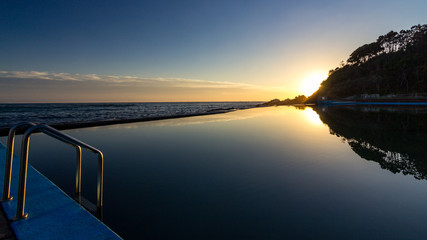 Fototapeta na wymiar Sun rising over ocean baths with reflection in water