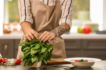 Woman preparing salad with fresh green basil at table
