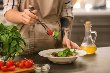 Woman preparing fresh salad with tomatoes and basil at table