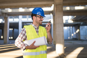 Male architect with blueprints using walkie-talkie