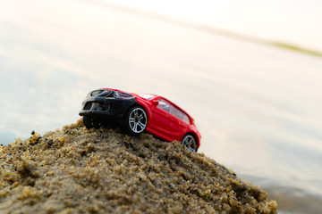 Fototapeta na wymiar toy car trying to call on a pile of sand on the beach, the littered horizon in the background of the sea