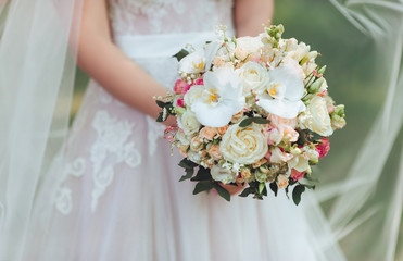 The bride in a white dress is holding a beautiful wedding bouquet in her hands. White orchids and roses. Delicate flowers.