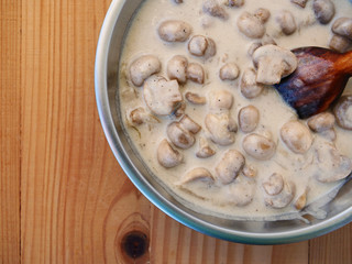 Creamy mushroom sauce for pasta in saucer pan over wooden table closeup, top view