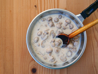 Creamy mushroom sauce for pasta in saucer pan over wooden table, top view