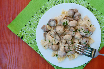 Farfalle pasta in creamy mushroom sauce on white plate top view