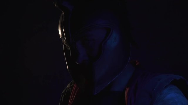 Male legionnaire in helmet slowly turns on camera in dark, slow motion