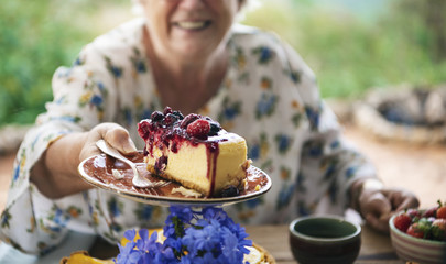 Grandmother holding a slice of cheesecake with mixed berries sauce © Rawpixel.com