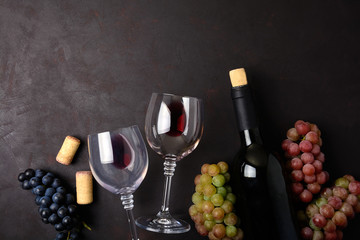 Wineglasses with red wine, bottle, grapes and corks lying on dark wooden background. Top view. Flat lay. Copy space