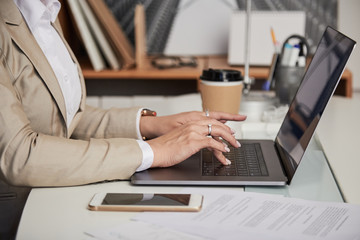 Crop side view of anonymous woman typing on laptop while working at table in office
