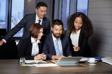 Group of multiracial men and woman gathering at table with laptop working in team on new project