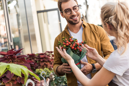 florist describing potted plant to happy customer near flower shop