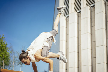 Attractive athletic man practicing yoga with maces outdoors in modern park.