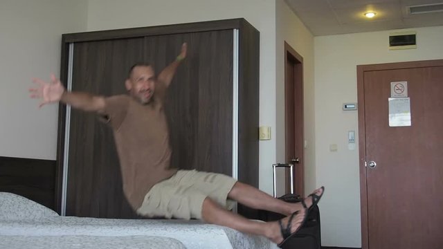 A man jumps on the bed. Tourist in hotel room jumping on the bed.